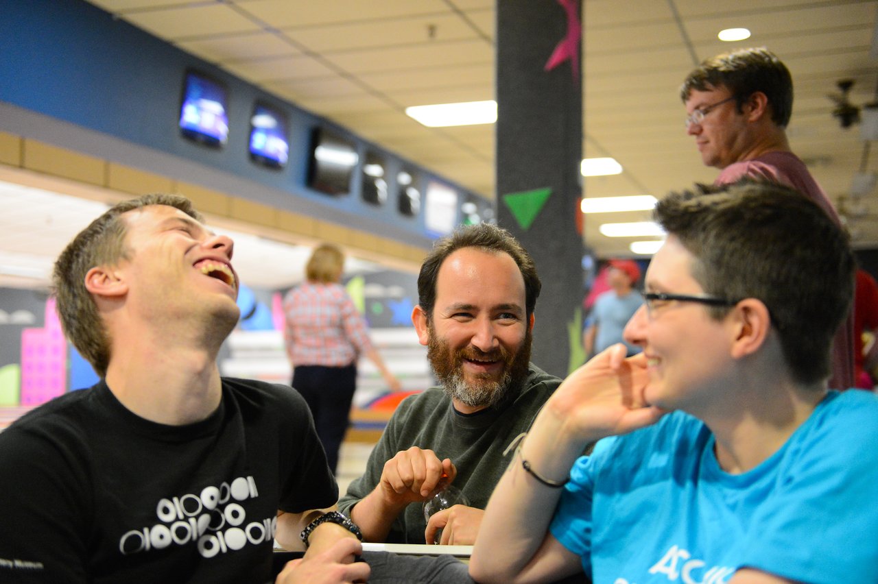 Three people are sitting together, laughing and talking at a bowling alley during Acquia Engineering Week 2012.