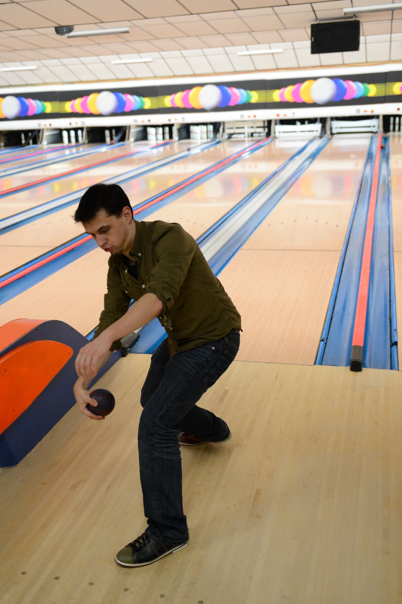 A person in a green shirt is bowling, releasing the ball down the lane at a bowling alley.