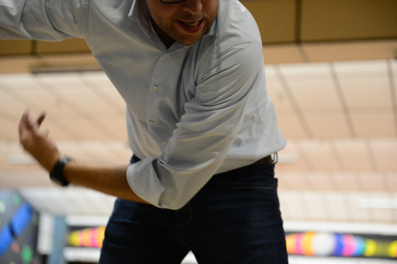 A person in a white shirt and glasses is mid-motion, possibly bowling, with a focused expression.