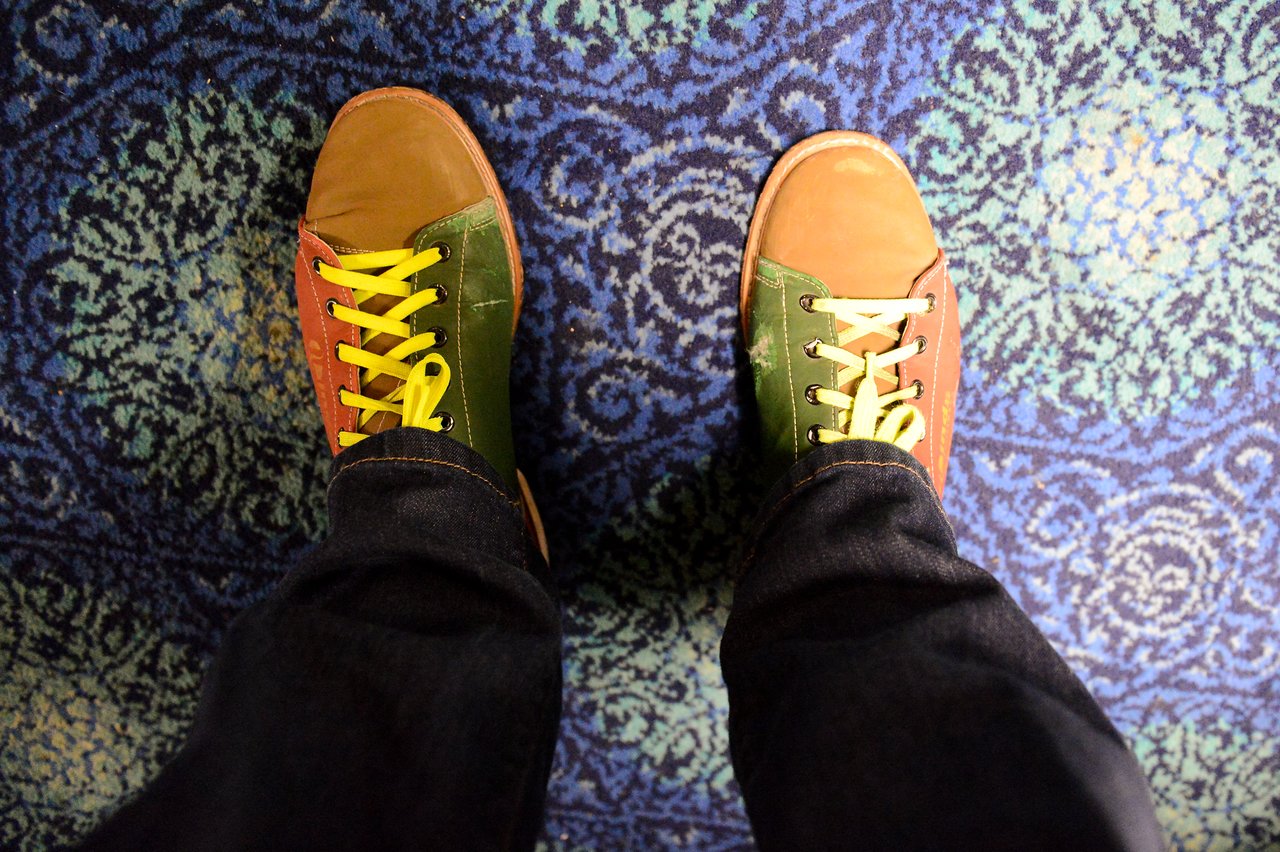 A person wearing colorful sneakers with yellow laces stands on a patterned blue carpet.