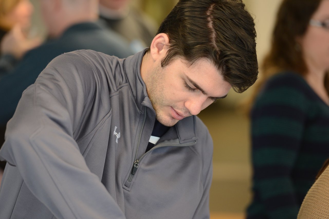 A man in a gray jacket looks down while focusing on an activity at an event.