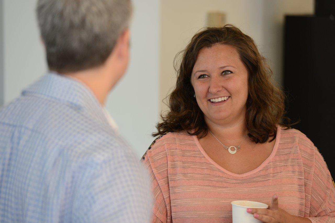 A woman holding a cup smiles while talking to a man at an Acquia executive breakfast event.
