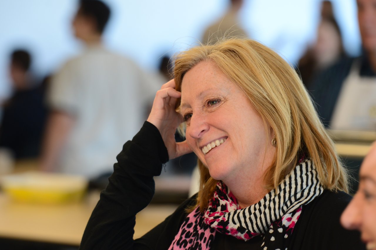 A woman with blonde hair and a patterned scarf smiles while engaged in conversation at a professional event.