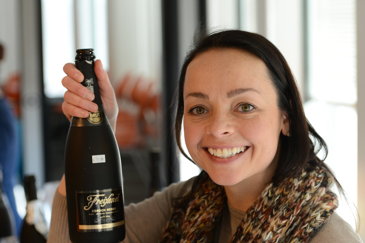 A smiling person holds up a bottle of Freixenet sparkling wine at an event.