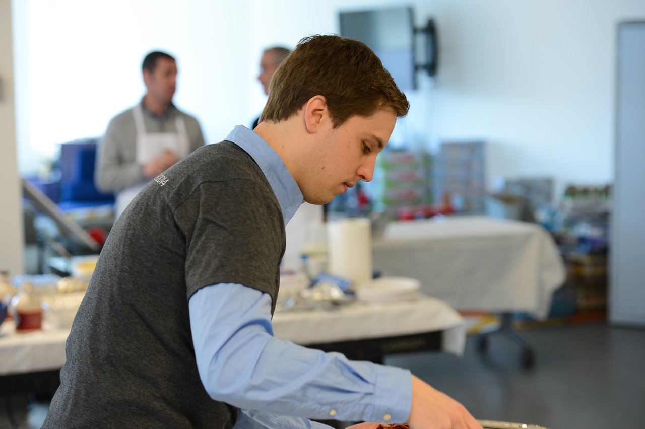 A man in a gray shirt serves food at a buffet table during an event.