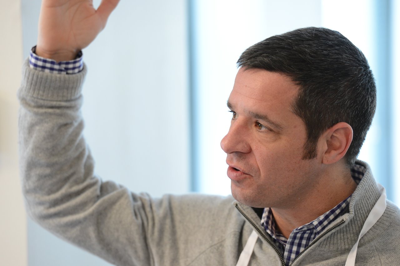 A man in a gray sweater raises his hand while speaking at the Acquia Executive Breakfast 2014.