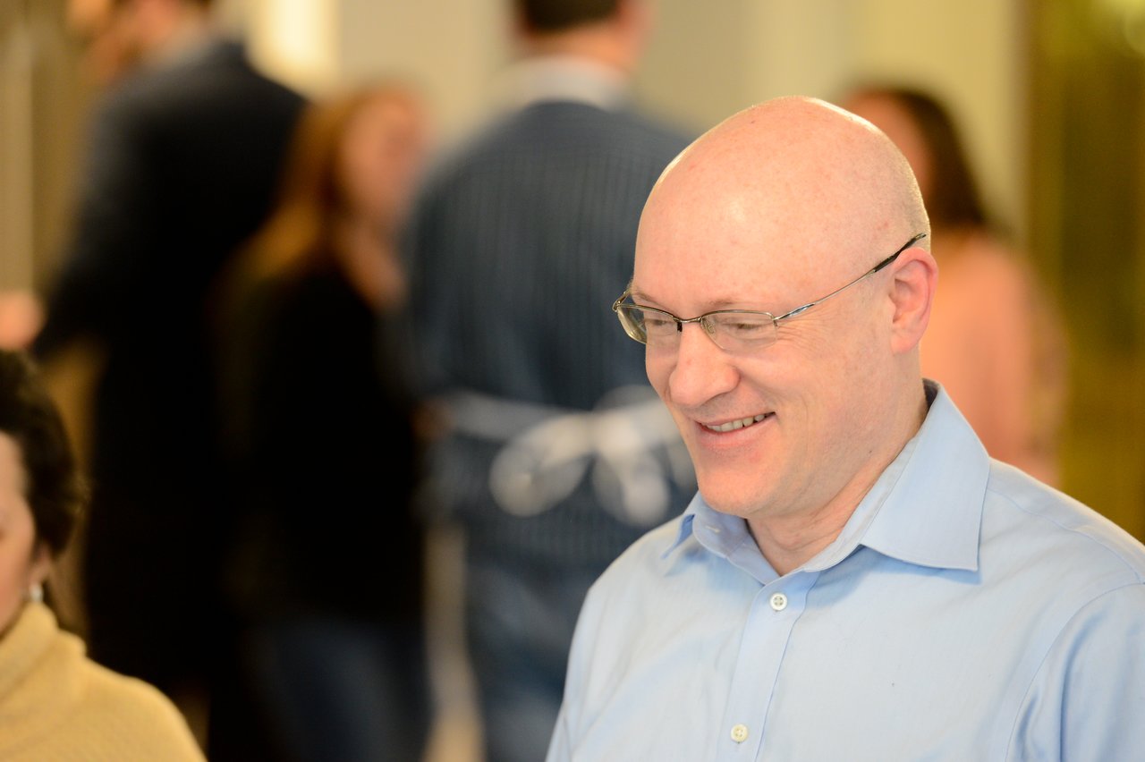 A man in a light blue shirt and glasses smiles while engaging in conversation at a professional event.