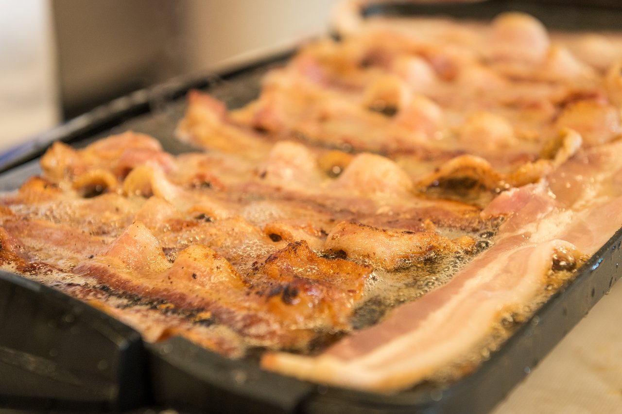 Bacon sizzling on a griddle, cooking in hot oil with crispy edges forming.