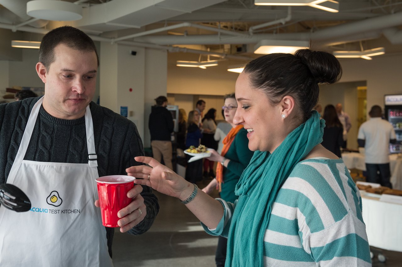 A man in an apron hands a red cup to a smiling woman at a breakfast event.