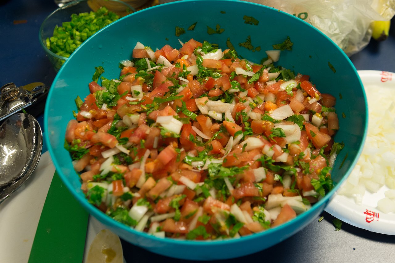 A blue bowl filled with freshly made pico de gallo, containing chopped tomatoes, onions, cilantro, and peppers.