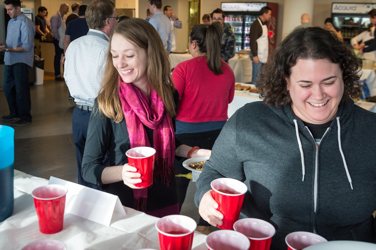 Two women smiling while holding red cups at a buffet table during a social event.