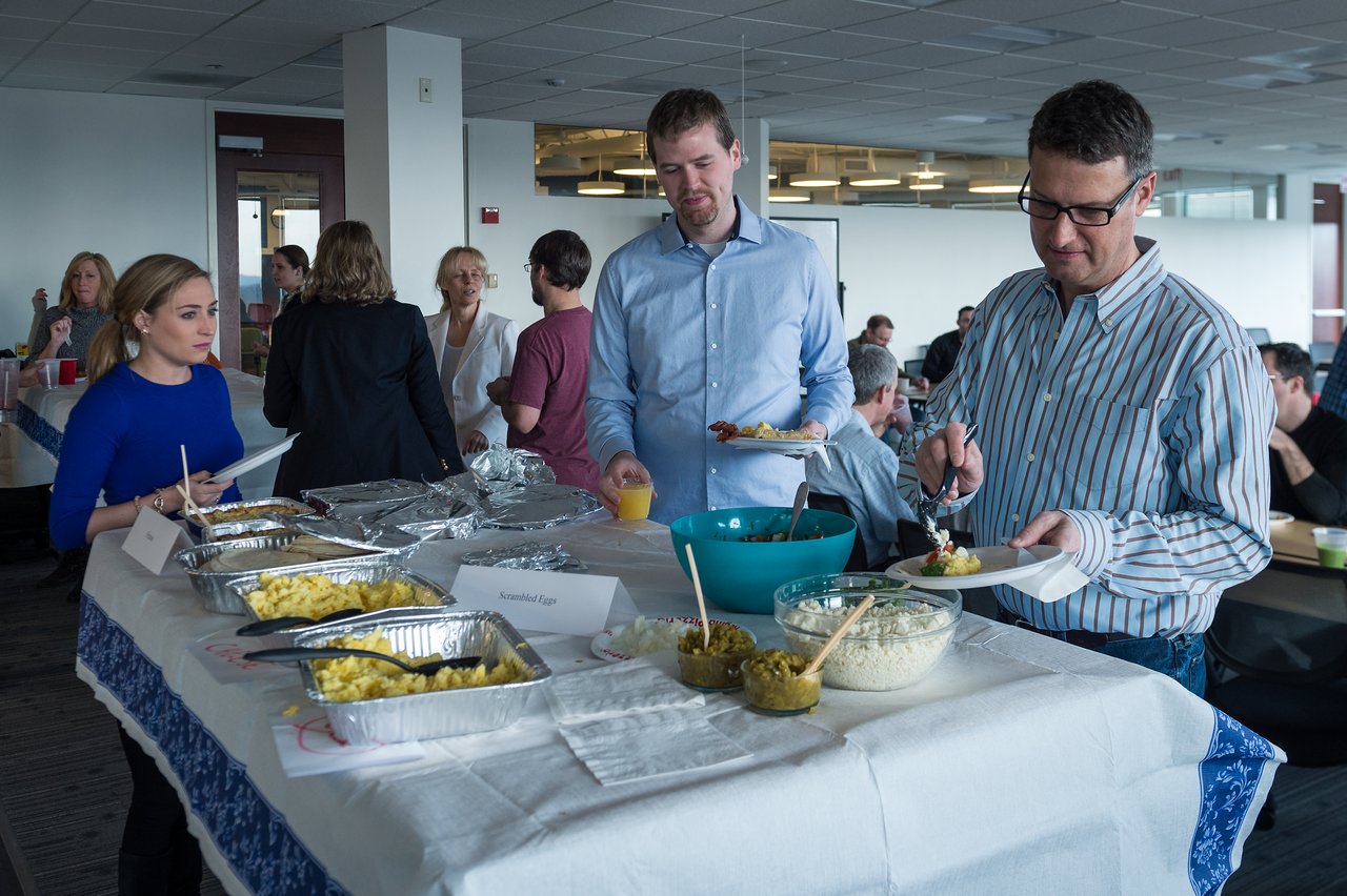 People serving themselves food from a buffet table at a corporate breakfast event in a well-lit office space.