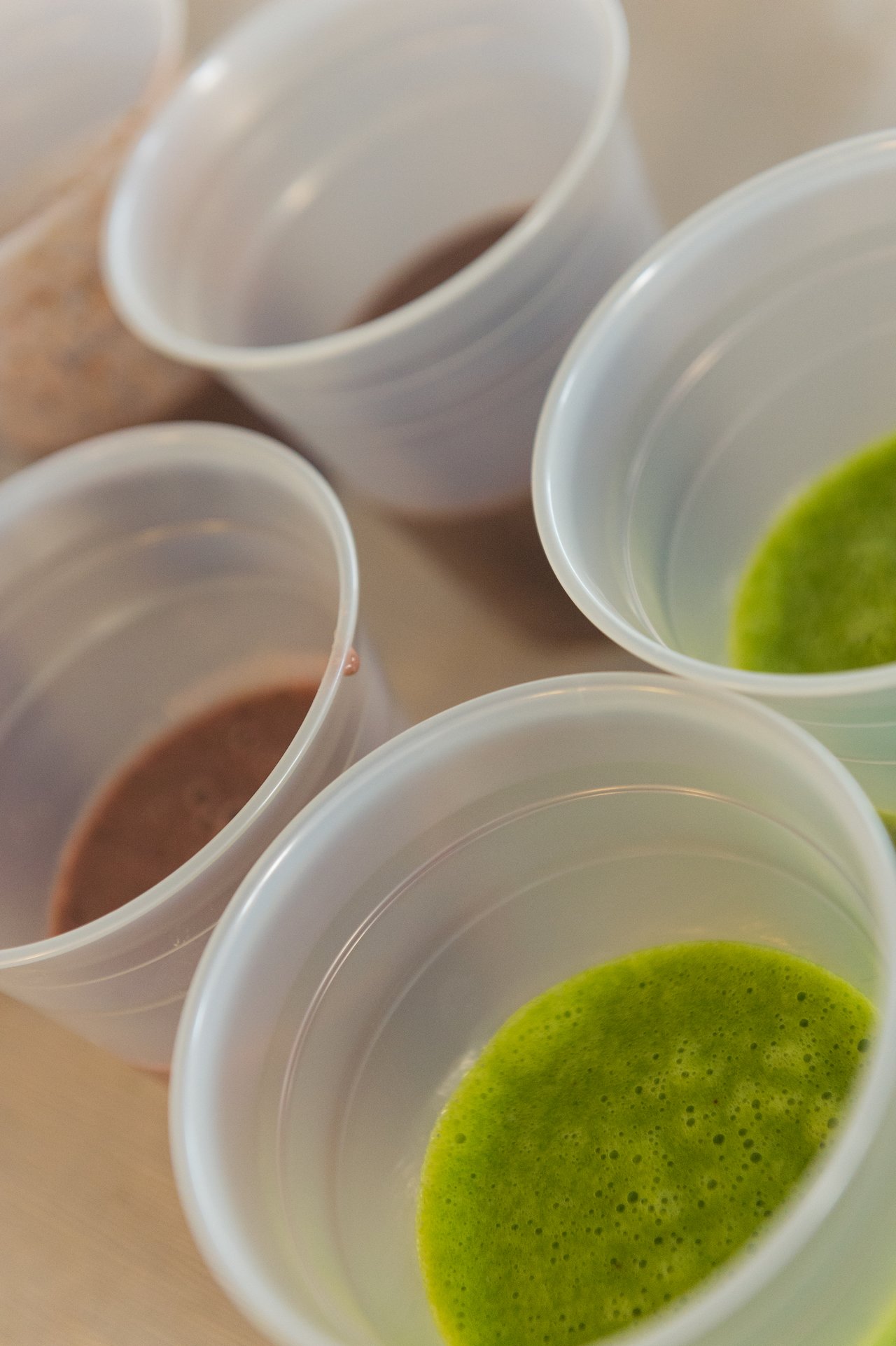 Several plastic cups filled with green and brown smoothies on a table.