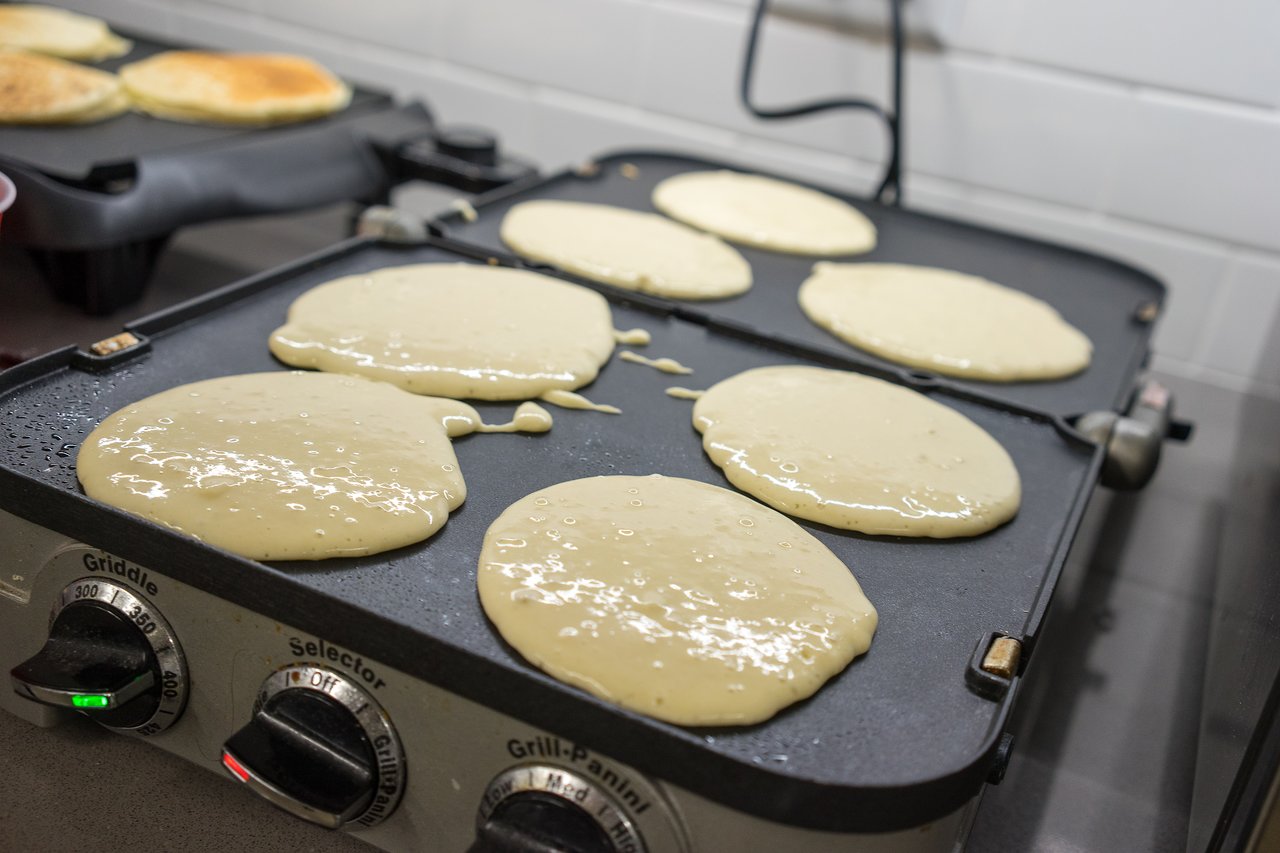 Pancake batter cooking on a griddle, with some pancakes already flipped and browning in the background.
