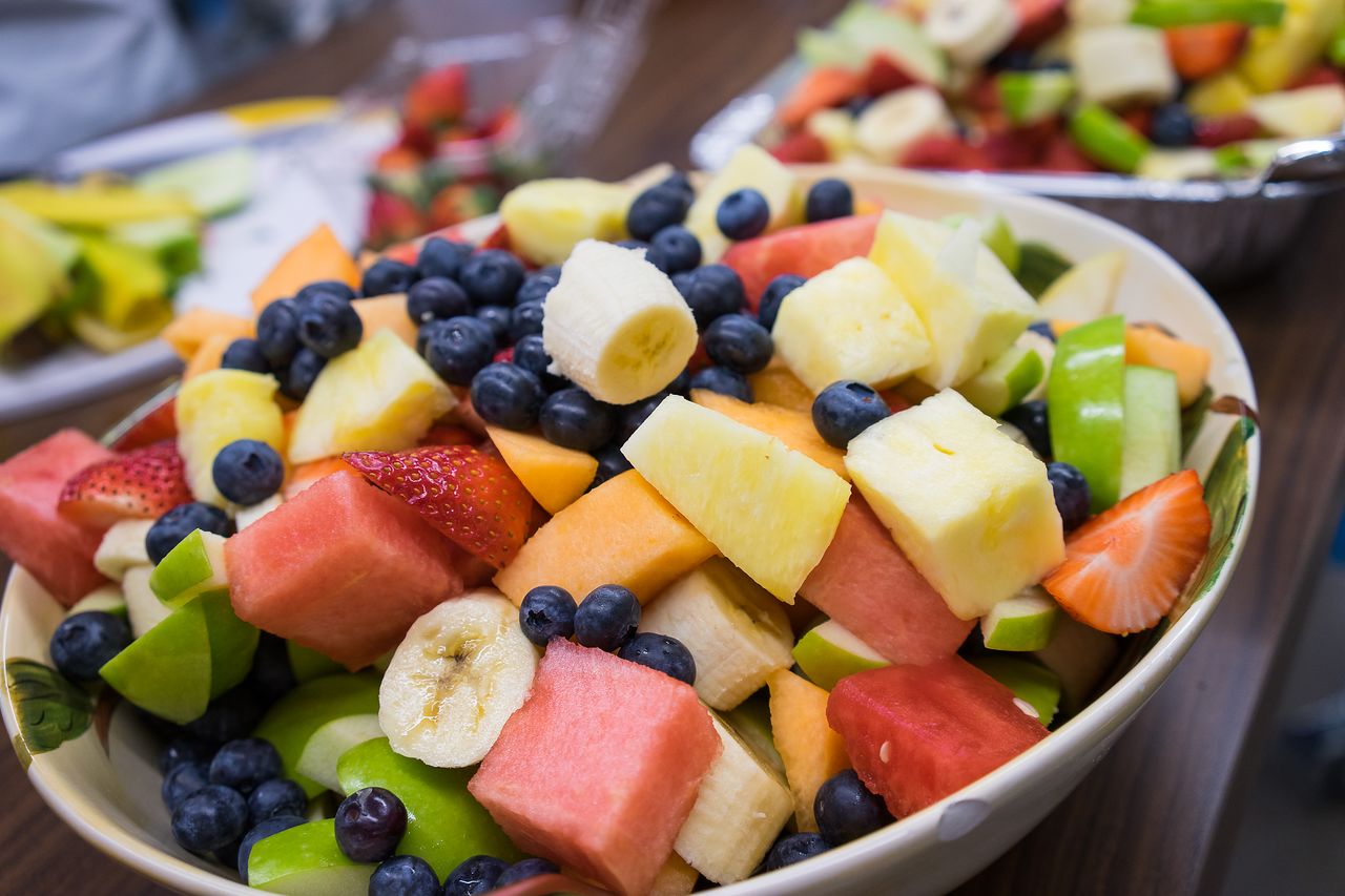 A bowl of mixed fresh fruit, including bananas, blueberries, watermelon, and pineapple, served at a breakfast event.