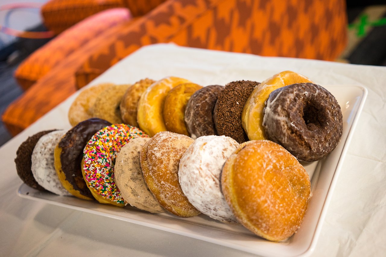A plate of assorted donuts, including glazed, powdered, and sprinkled varieties, arranged on a table.