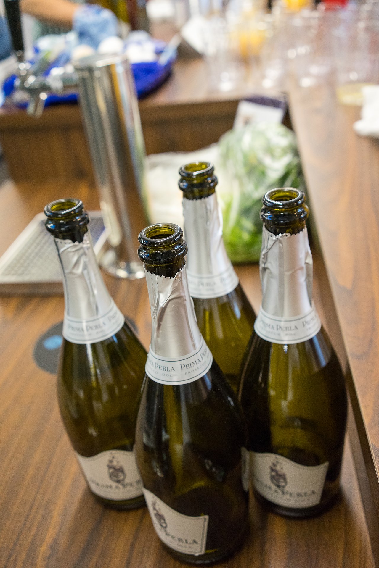 Four empty champagne bottles on a wooden bar counter, with glasses and ingredients in the background.