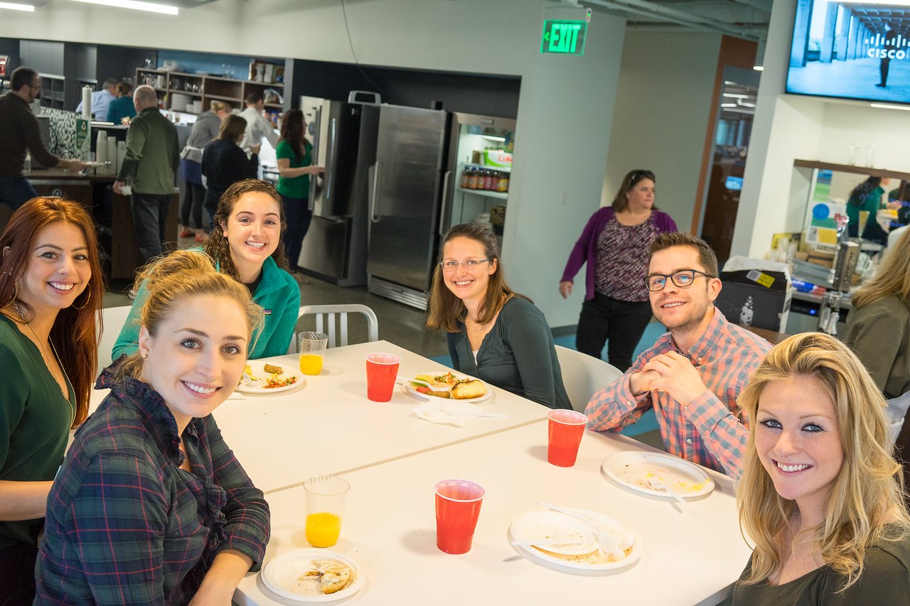 A group of people sitting at a table, smiling and enjoying a meal together at a casual gathering.
