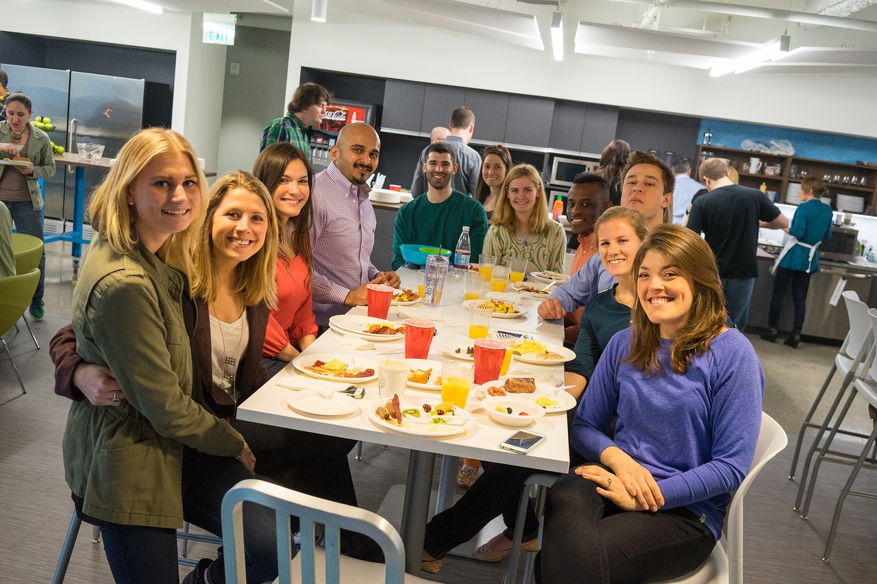 A group of people sitting at a table, smiling and enjoying breakfast together in a casual setting.