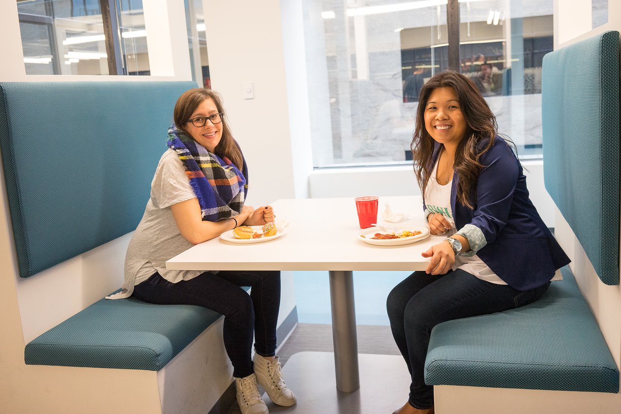 Two women sitting at a booth, smiling and eating breakfast at an Acquia event.