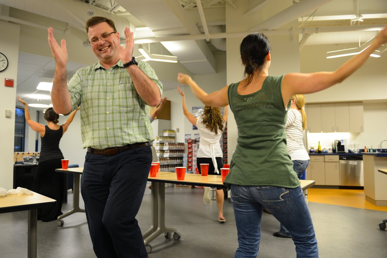 People are dancing and having fun at an indoor party, with red cups on tables in the background.