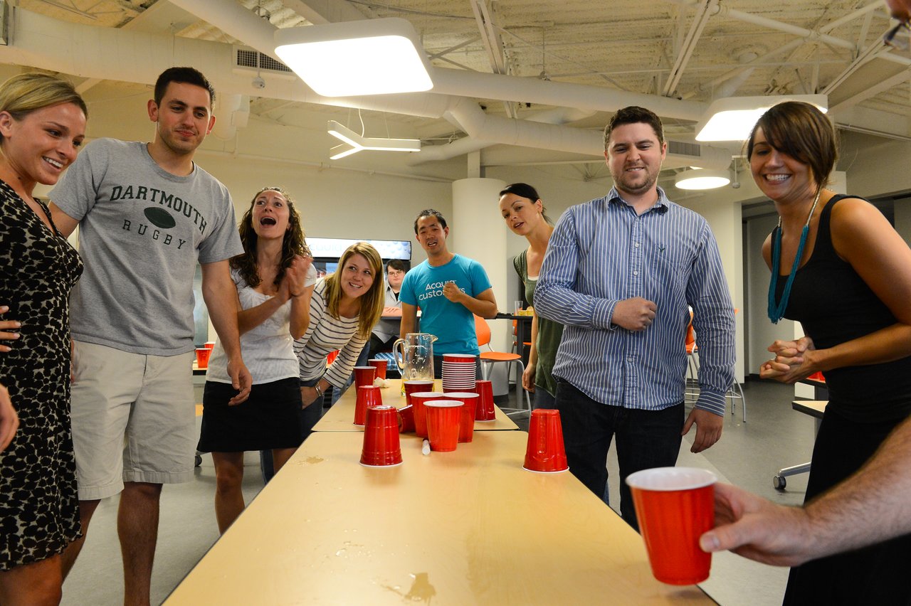 A group of people laughing and cheering while playing a cup-flipping game at a party.
