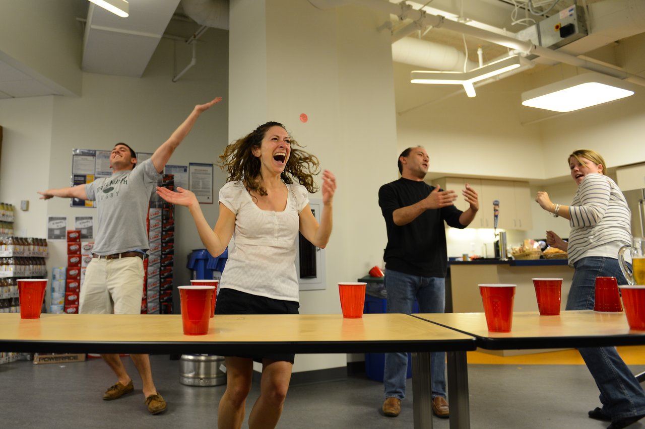 People are playing a party game with red cups, reacting with excitement and laughter in an indoor setting.