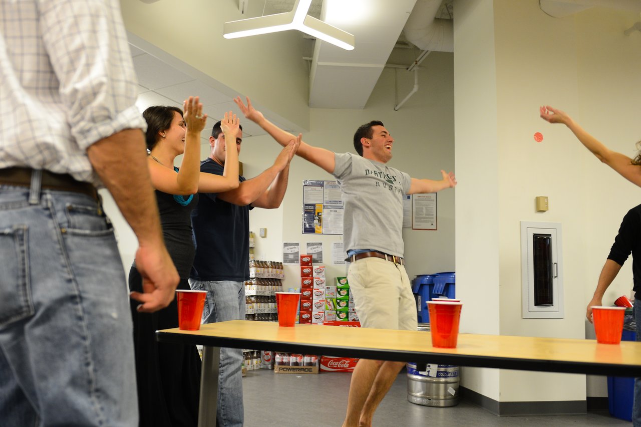 A group of people celebrate and cheer while playing a party game with red cups on a table.