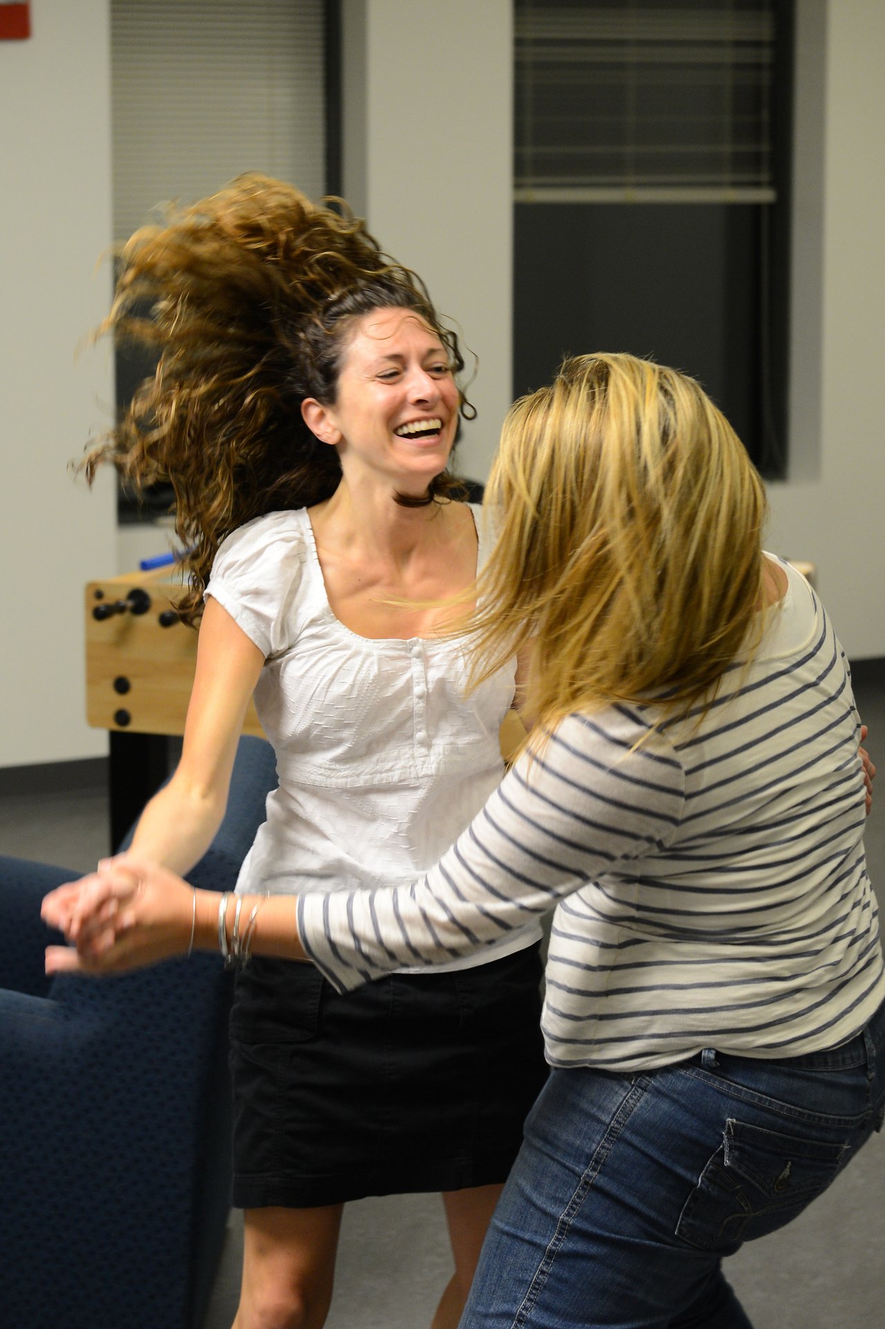 Two women dancing together, smiling and holding hands in an indoor setting.