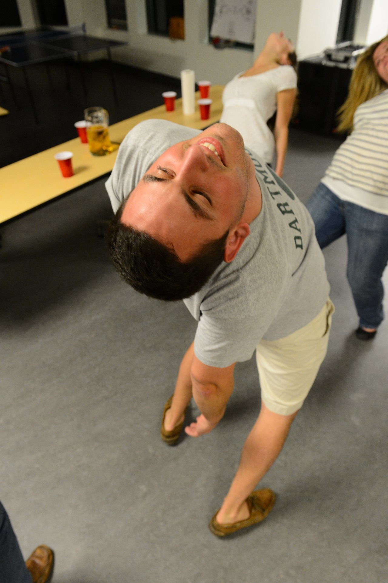 A man leans back while playing limbo at a party, with others participating in the background.