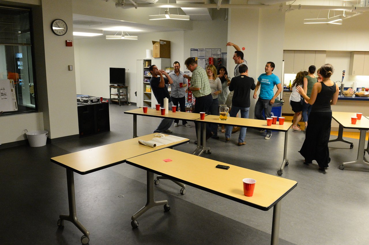 A group of people socializing and playing drinking games in an indoor party setting with red cups on tables.