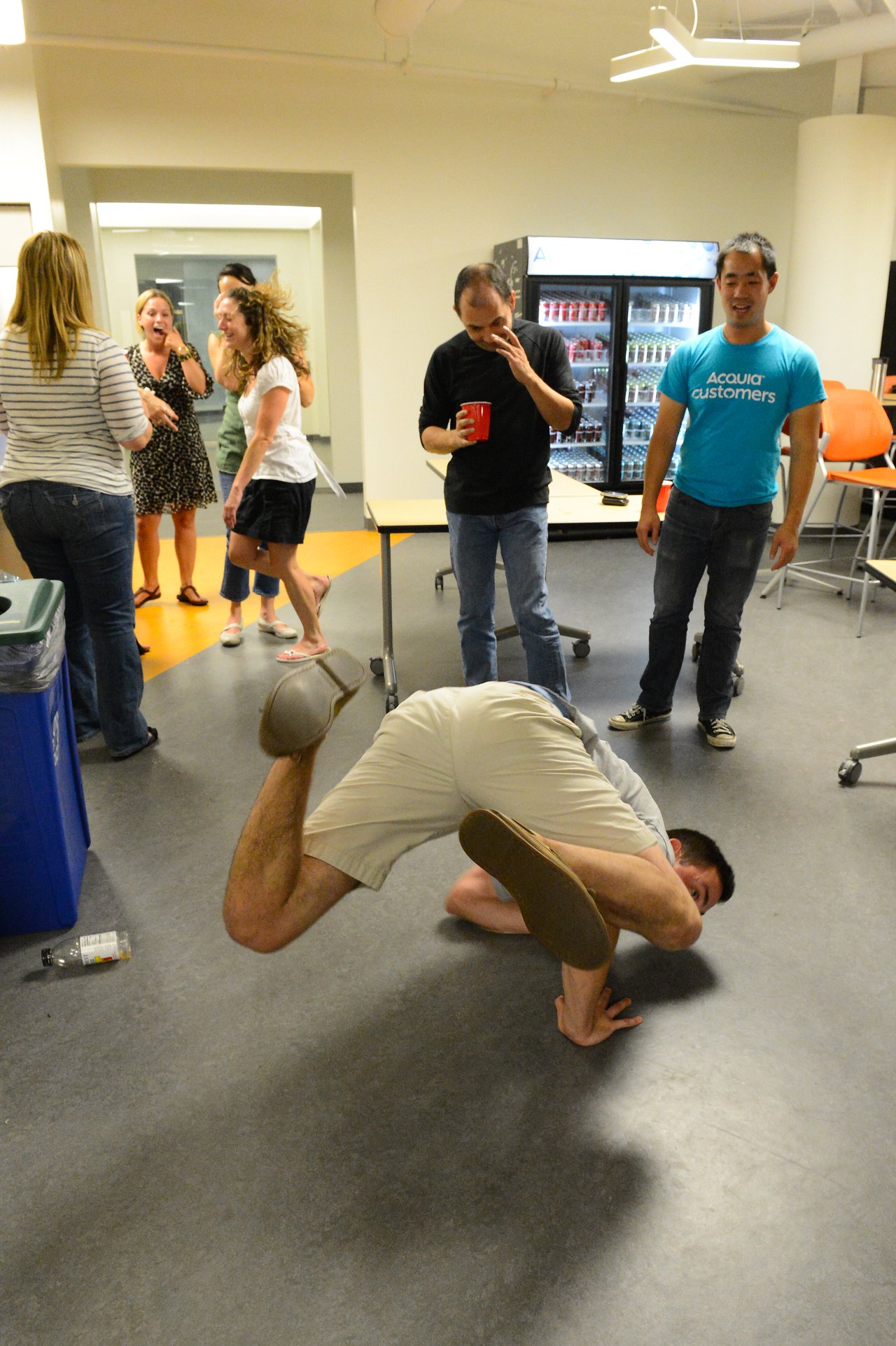 A man performs a breakdancing move on the floor while others watch and laugh at a party.