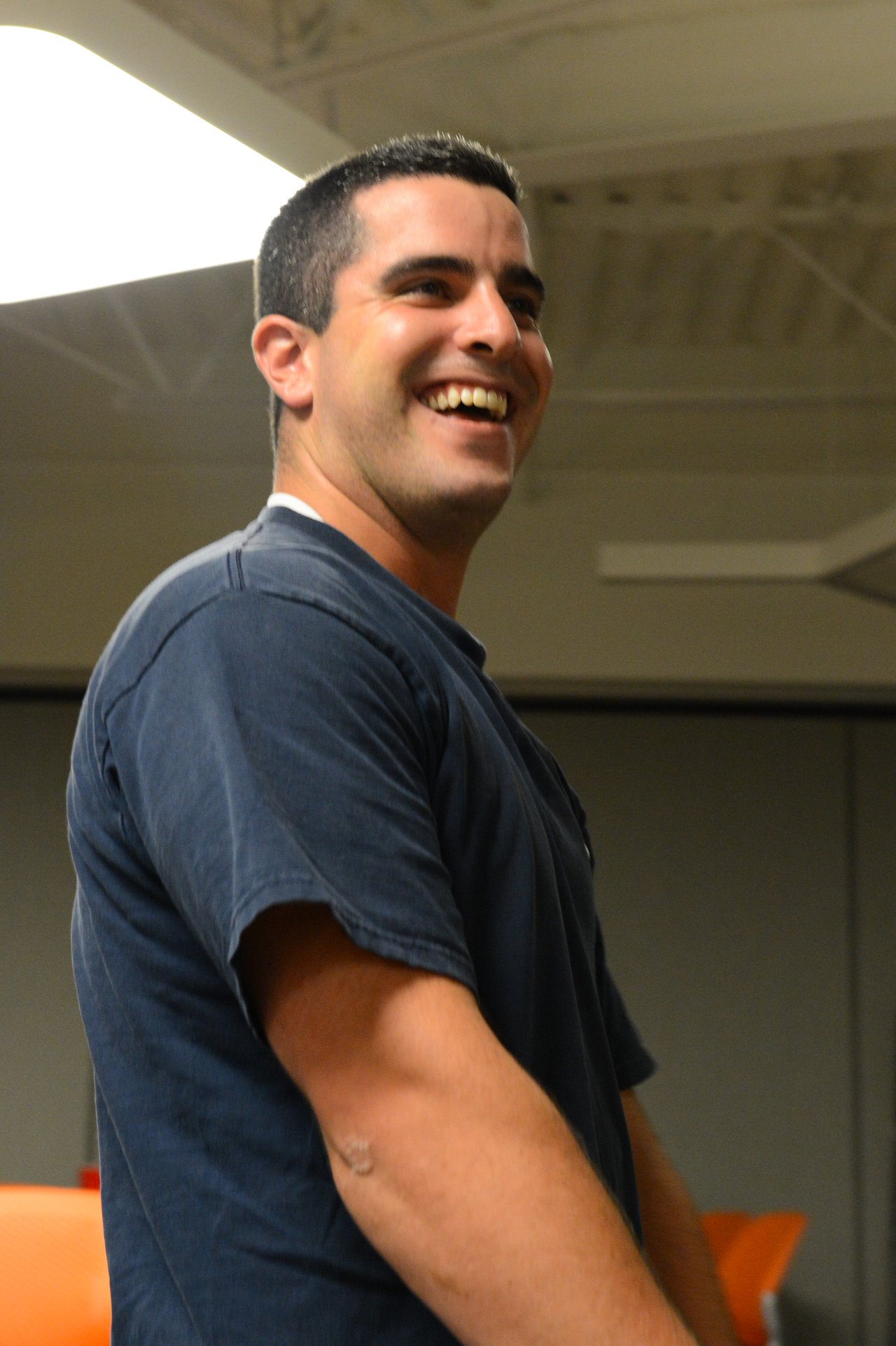 A man in a dark t-shirt smiles and laughs at an indoor party.