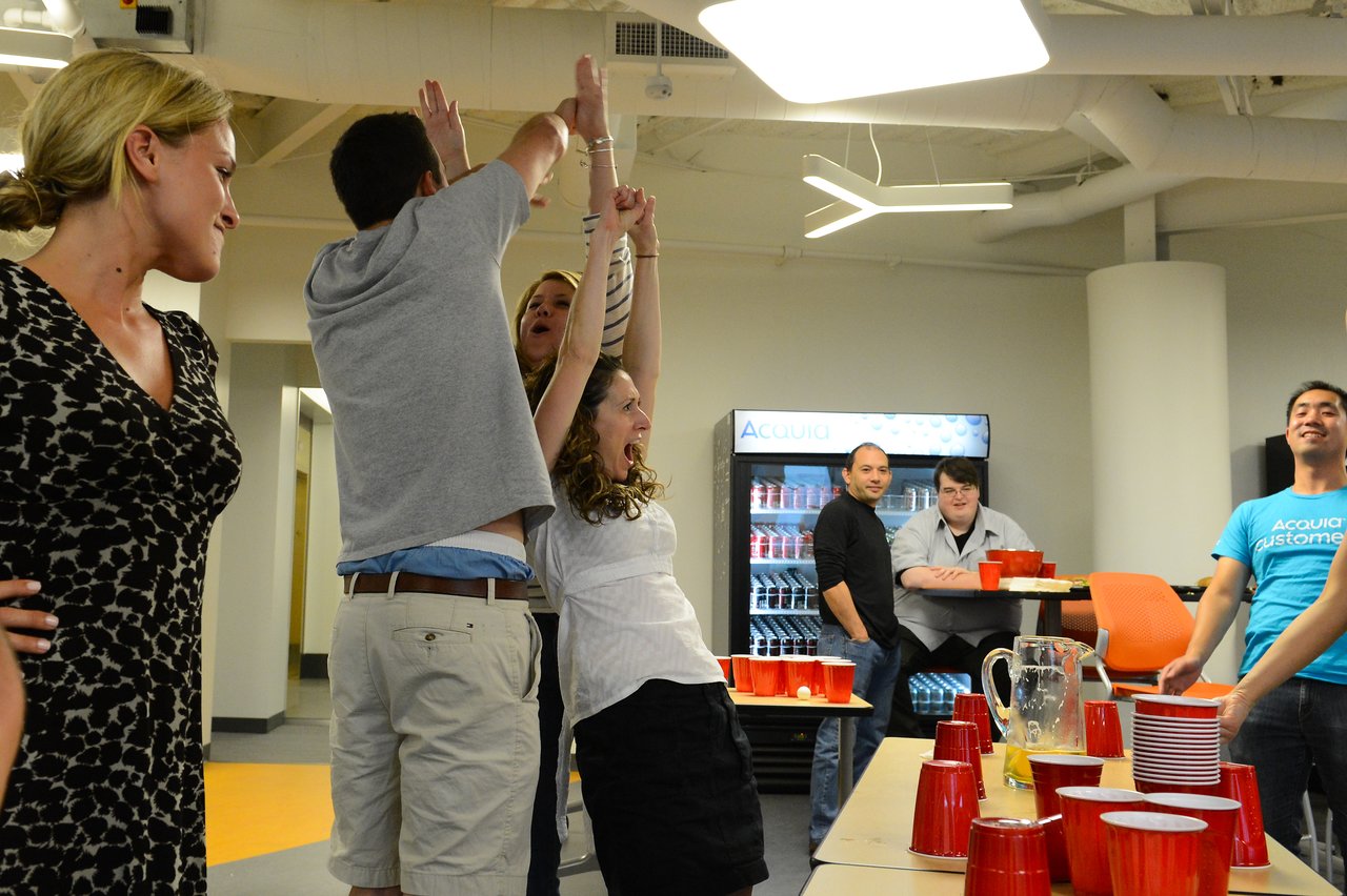 People celebrating at a party, with two individuals raising their hands in excitement near a table with red cups.