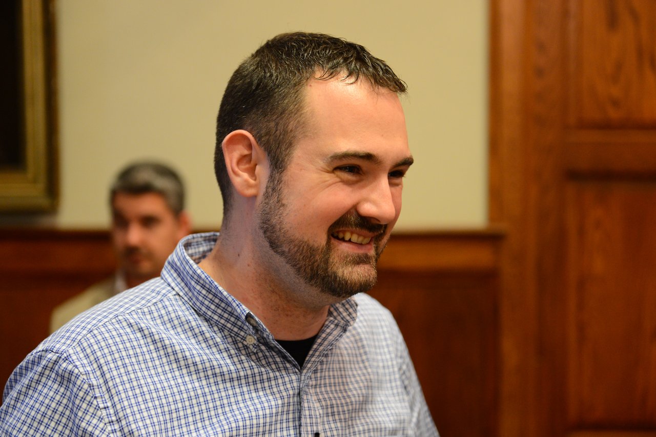 A man in a checkered shirt smiles while engaged in conversation at an indoor event.
