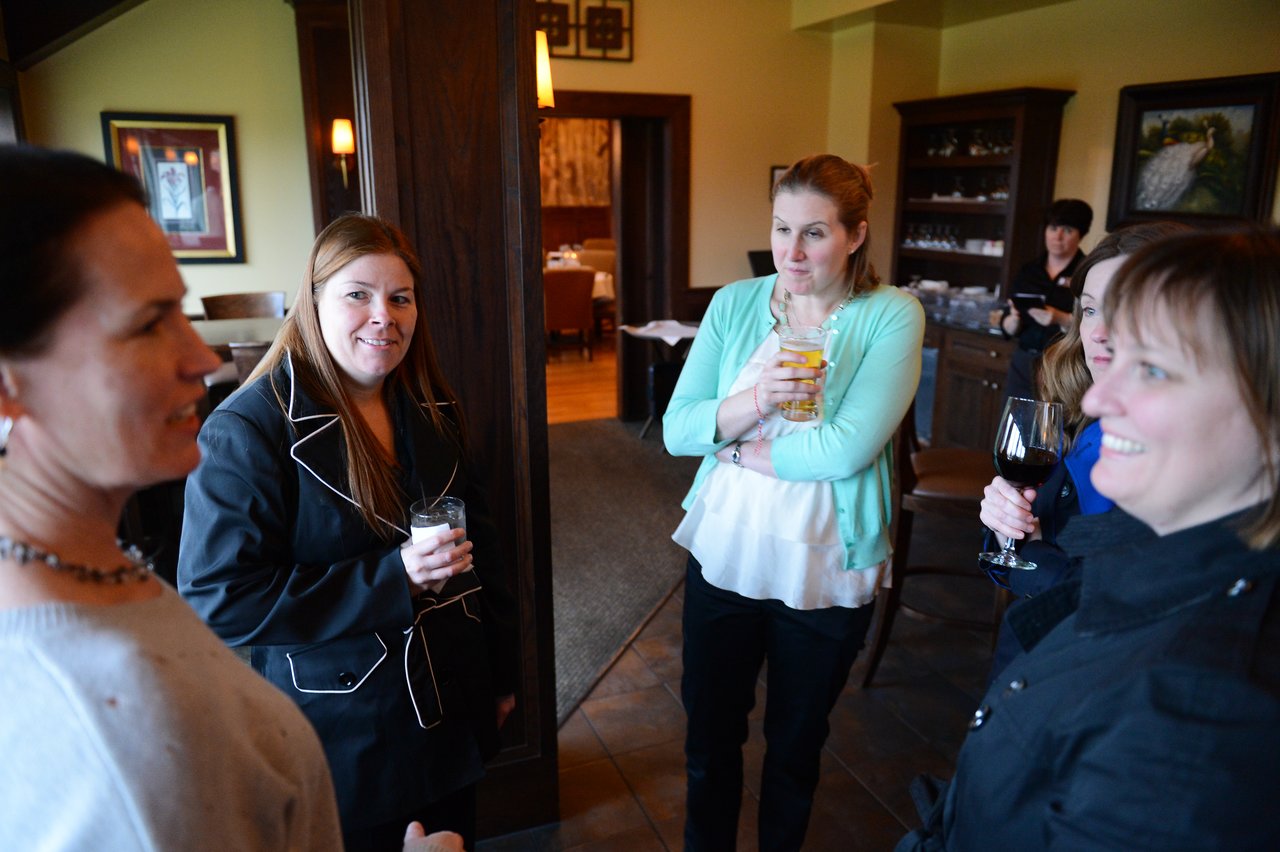 A group of women stand in a restaurant, holding drinks and engaged in conversation.