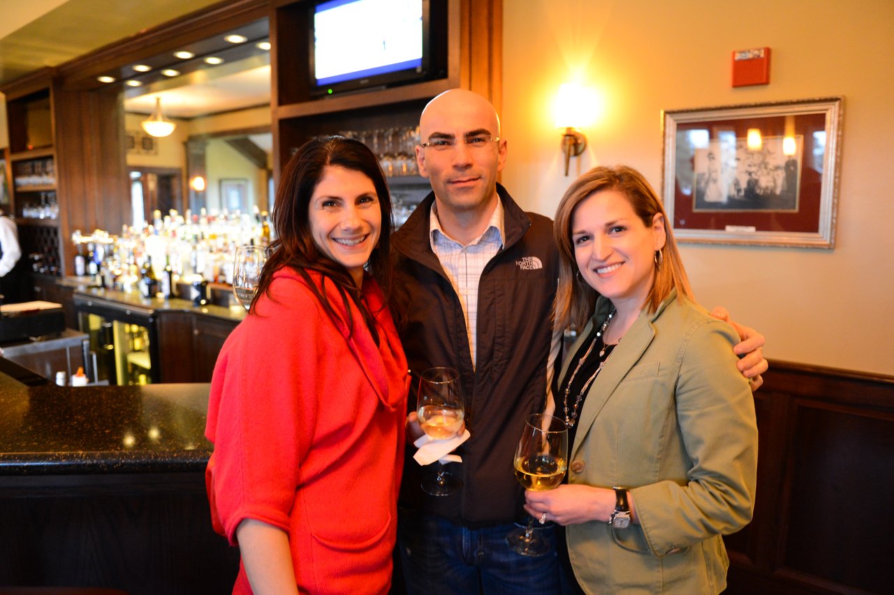 Three people stand together in a bar, smiling and holding wine glasses during an Acquia offsite event.