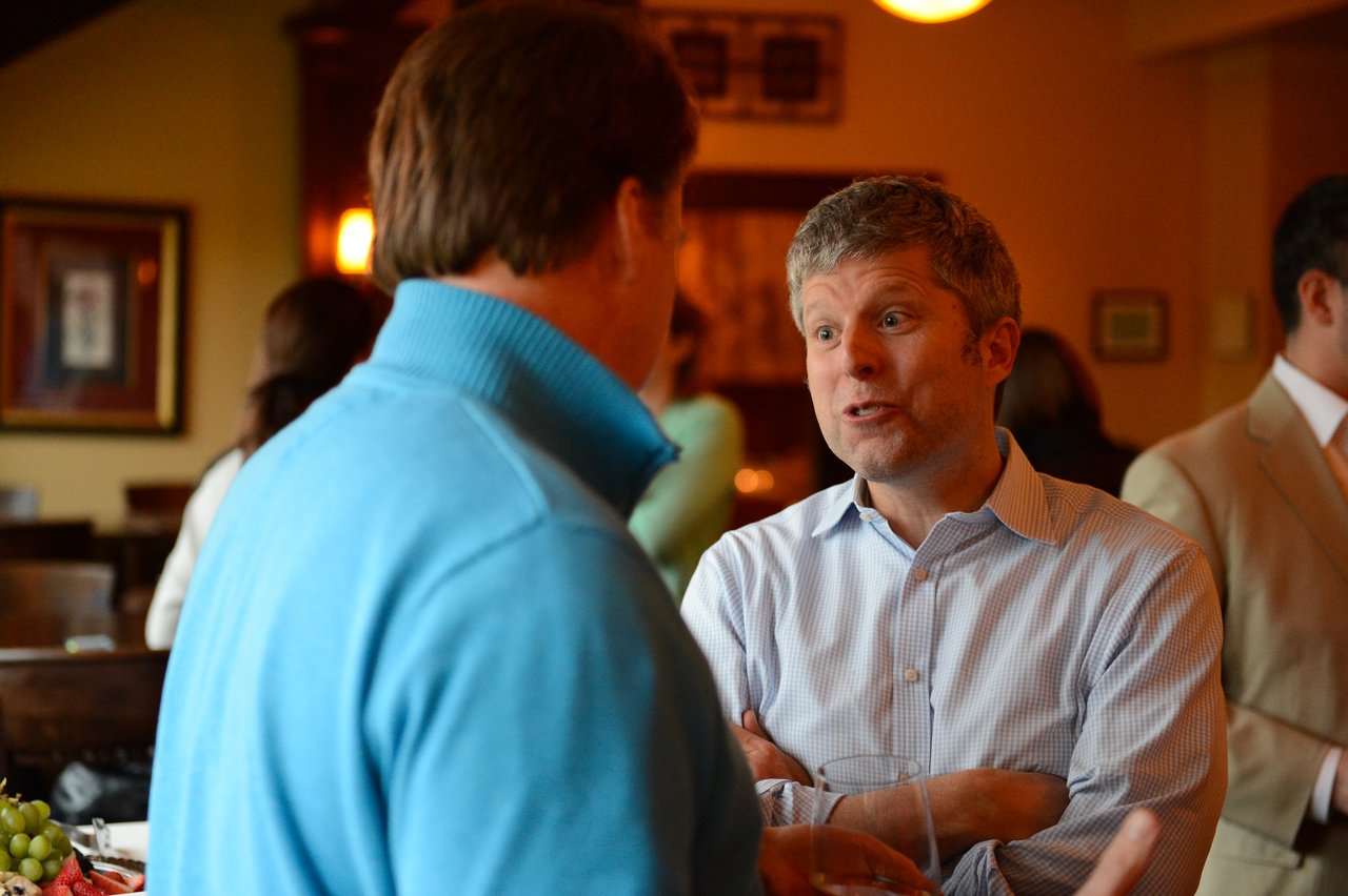 Two men engaged in conversation at a social gathering, with one gesturing while speaking.