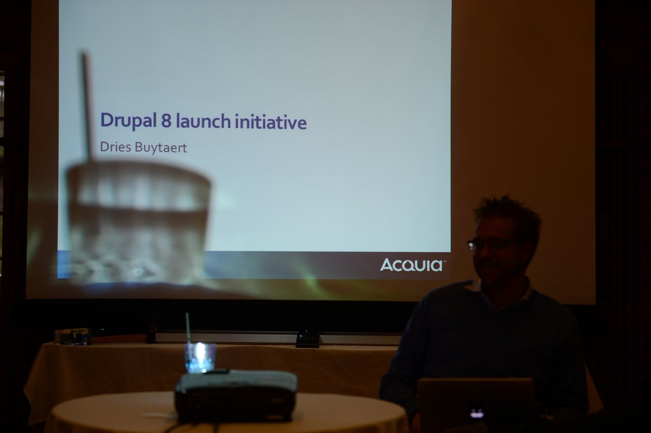A presentation slide titled "Drupal 8 launch initiative" is displayed, with a speaker sitting in front of it.