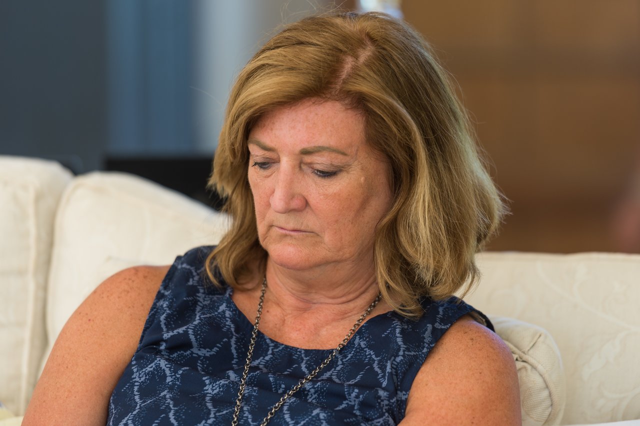 A woman with shoulder-length hair sits on a couch, looking down with a focused expression.