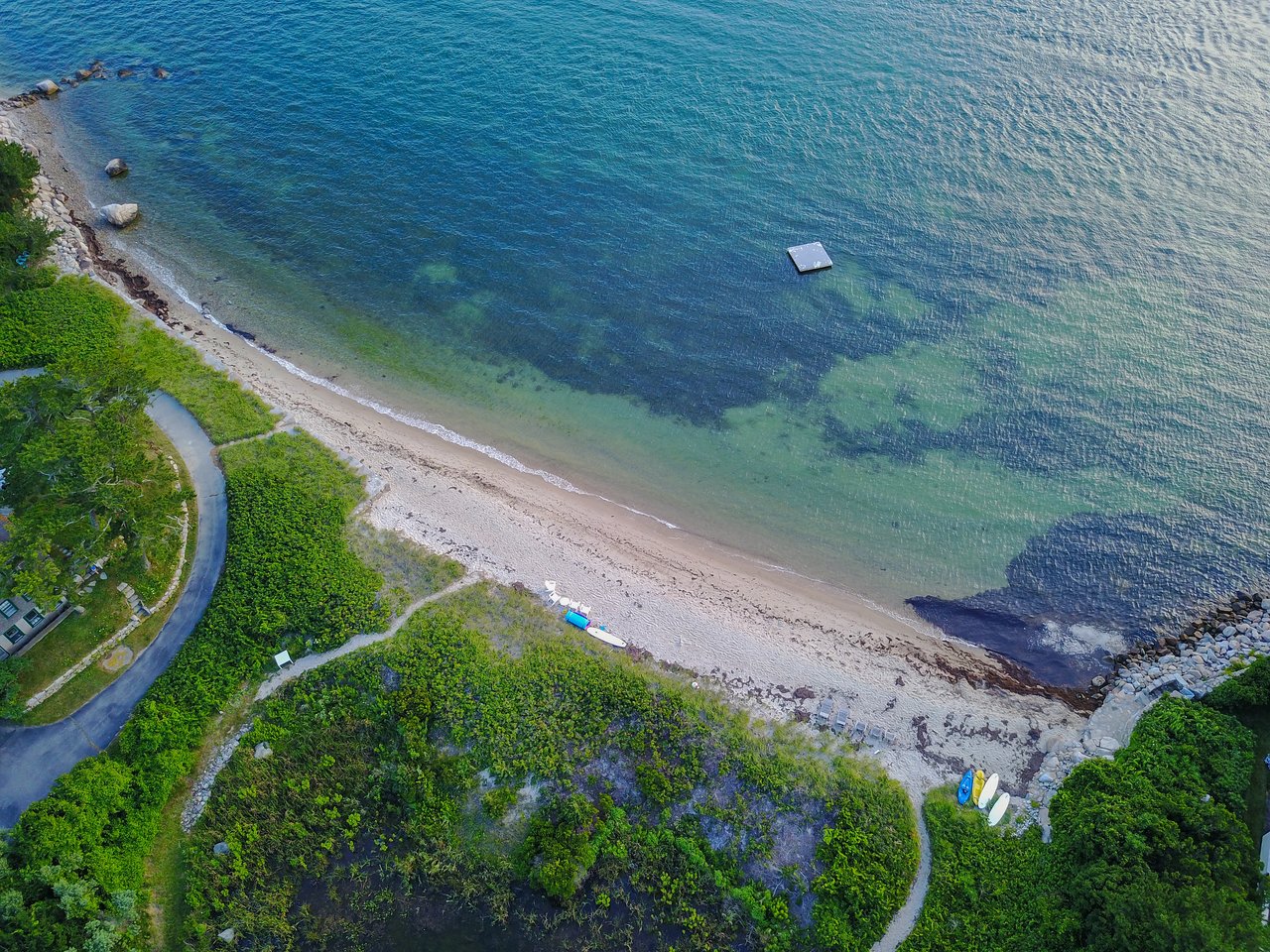 Aerial view of a sandy beach with small boats onshore and a floating platform in the clear water.
