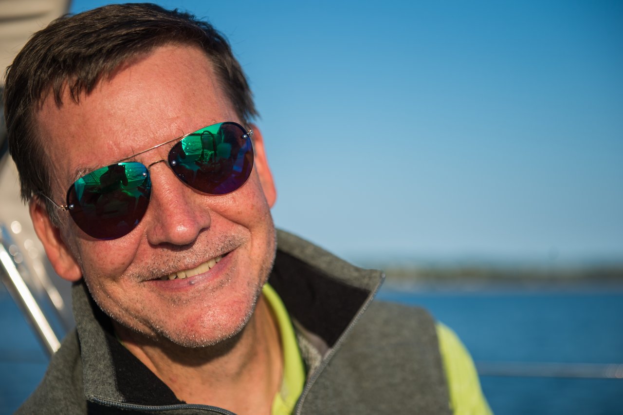 A man wearing sunglasses and a vest smiles while sailing on the water at Martha's Vineyard.