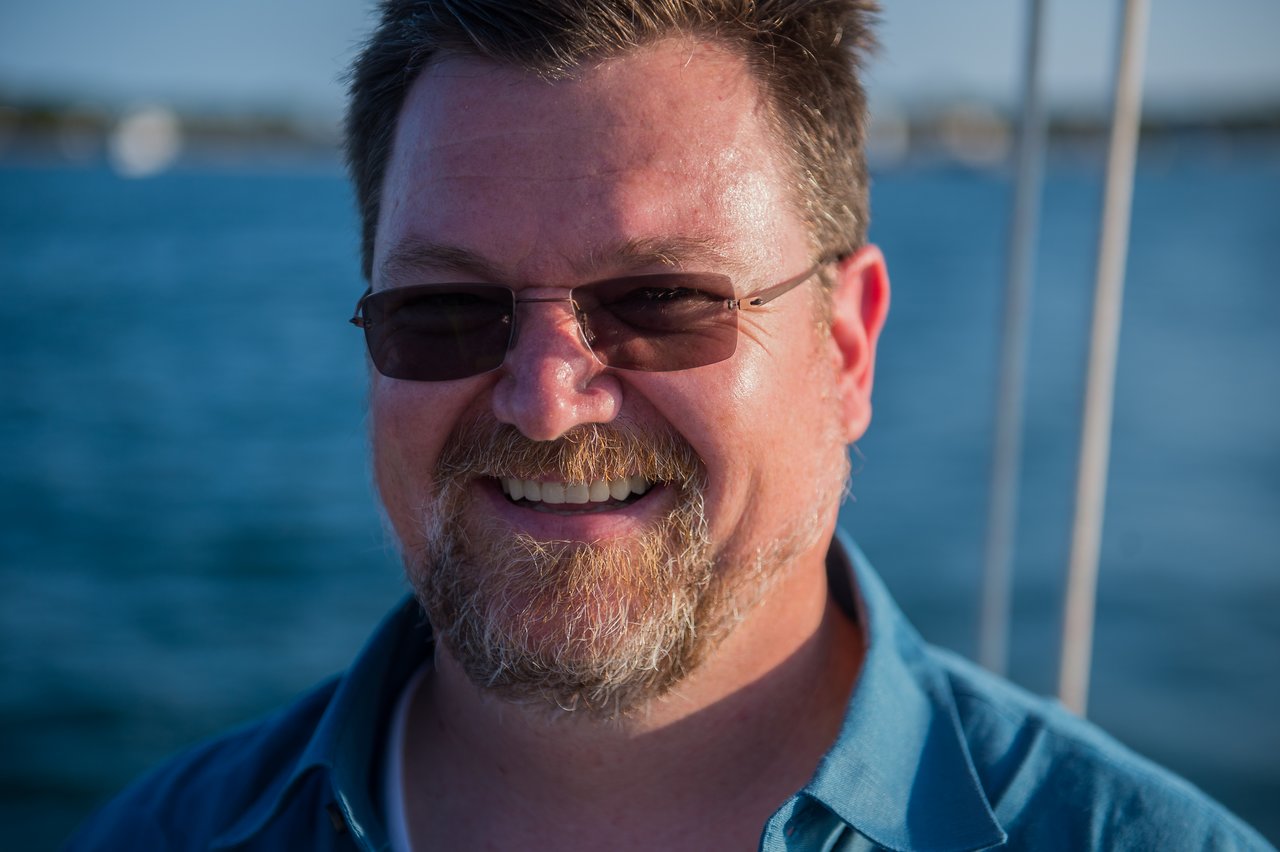 A man wearing sunglasses and a blue shirt smiles while sailing on the water at Martha's Vineyard.
