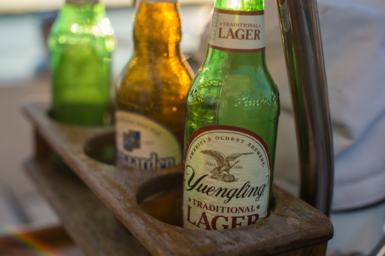 Three beer bottles in a wooden holder on a boat, with a Yuengling Lager bottle in focus.