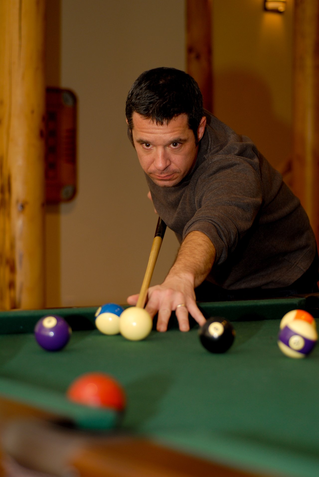 A man in a dark sweater leans over a pool table, aiming his shot with a cue stick.