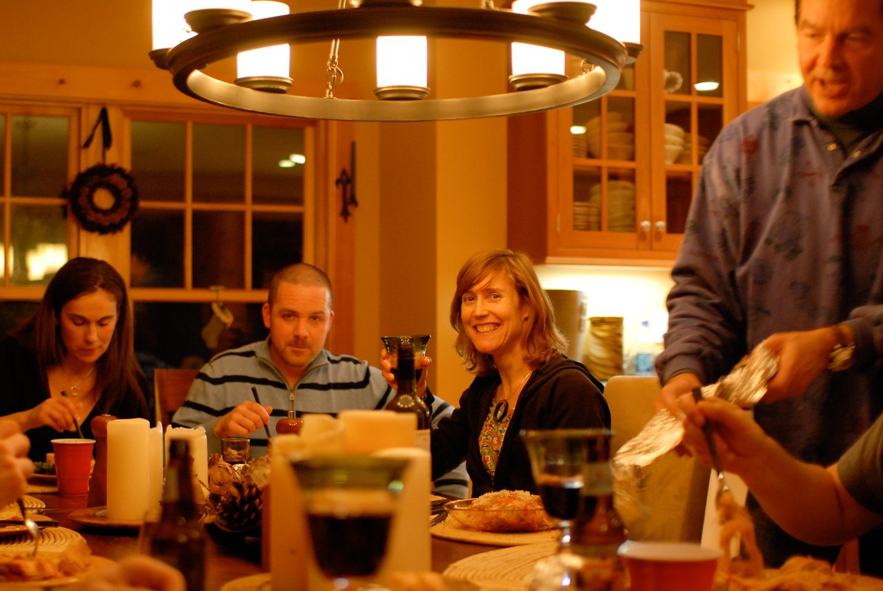 A group of people gathered around a dinner table, eating and drinking in a warmly lit setting.