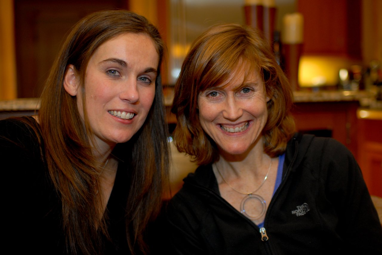 Two women smiling at the camera in an indoor setting with warm lighting.