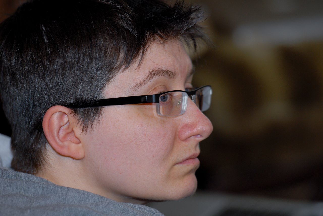 A person wearing glasses and a gray shirt looks attentively to the side in an indoor setting.