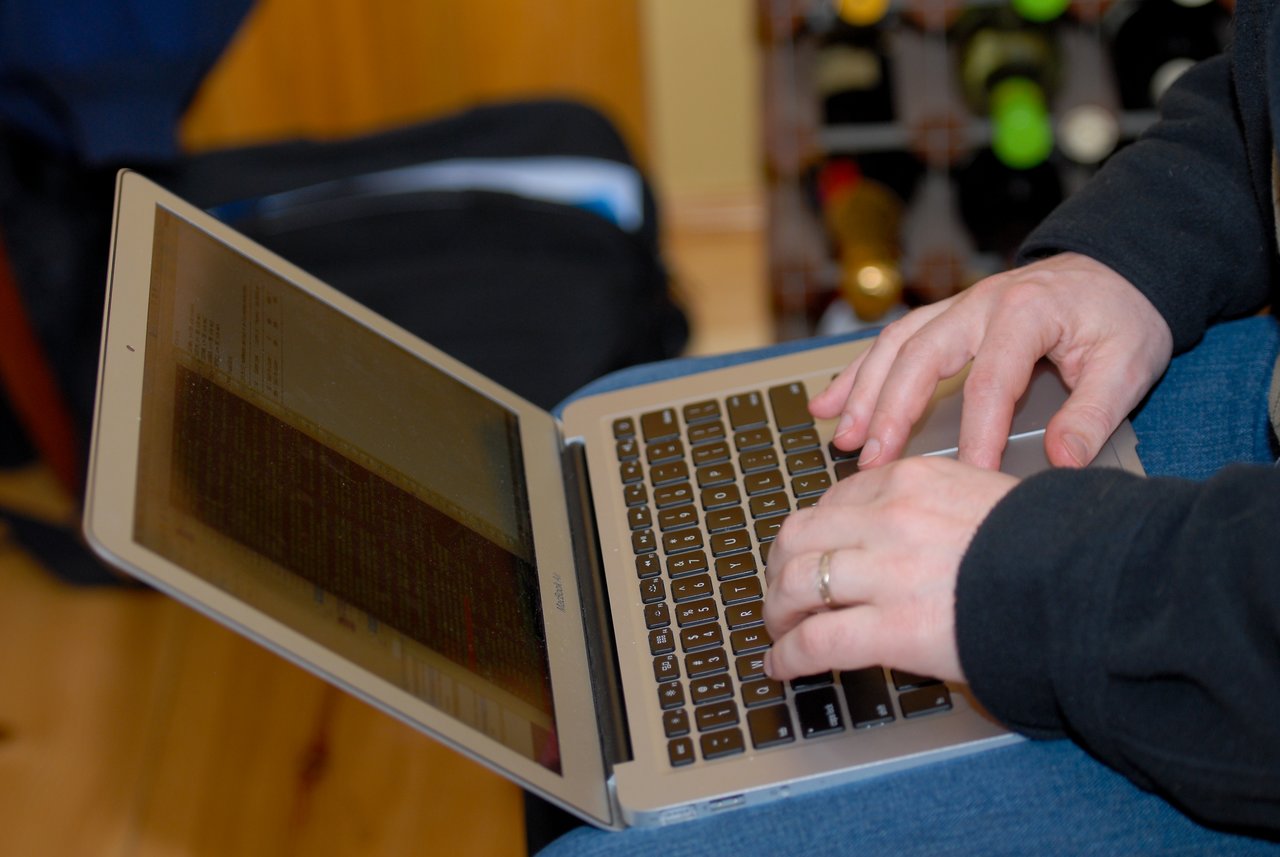 A person types on a laptop with a screen displaying code or text.