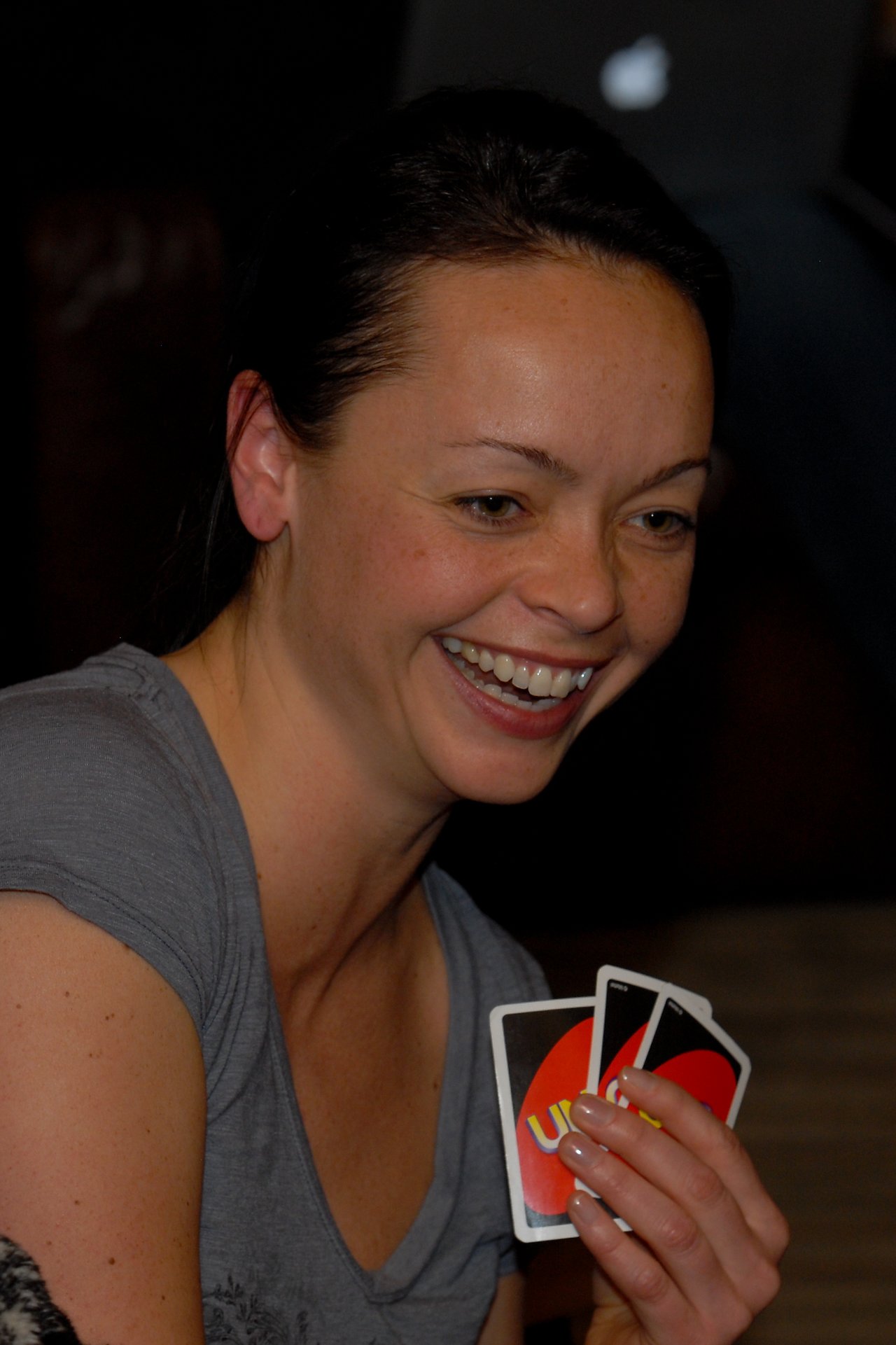 A woman smiles while holding Uno cards during a game.